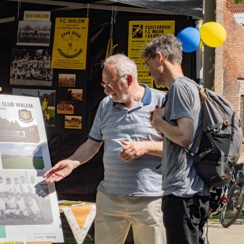 Bezoeker krijgt uitleg bij informatiebord van KFC Walem terwijl bestuurslid dingen aanwijst.