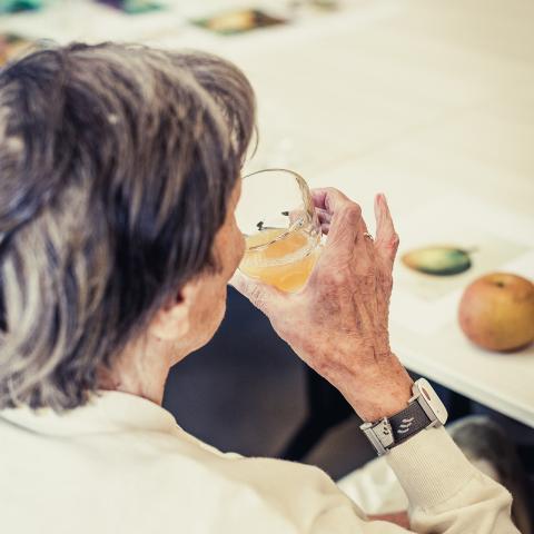 Vrouw met zwart haar houdt een glas vast met appel of perensap, ze maakt aanstalten om ervan te drinken